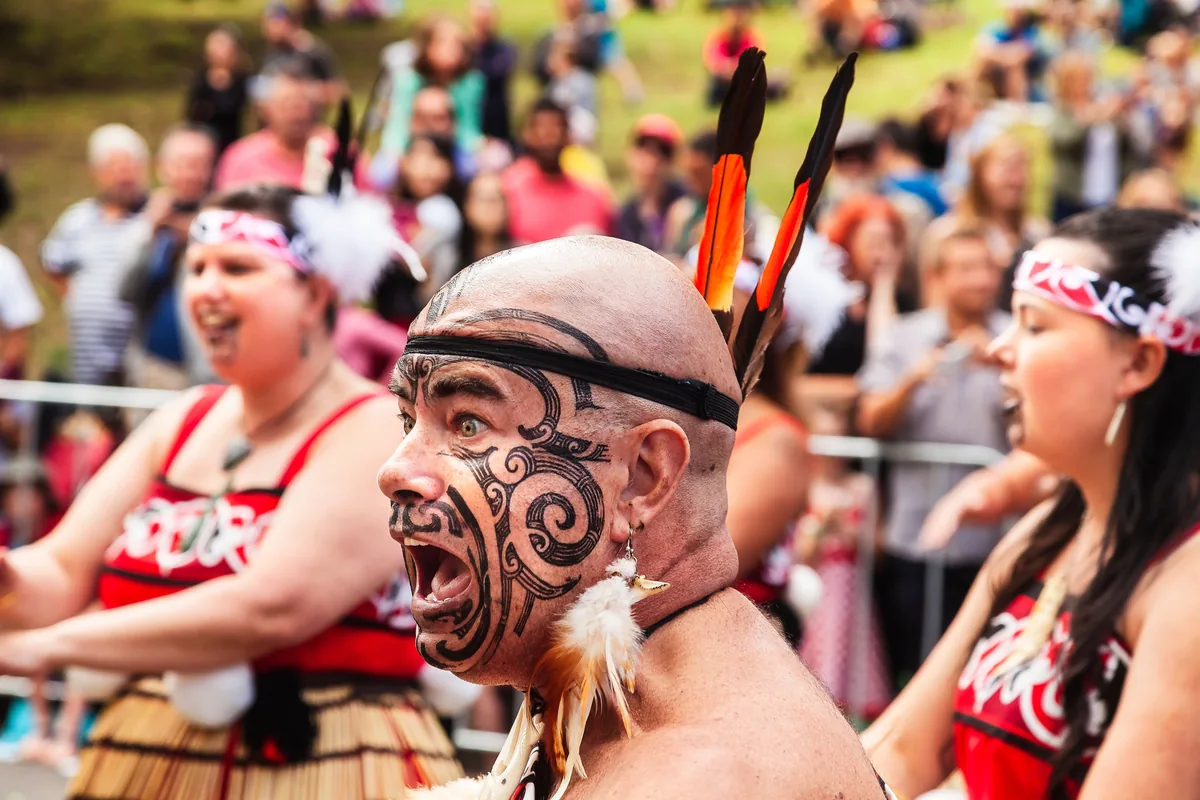 A Maori performer with traditional ta moko facial markings performing at a daylight festival